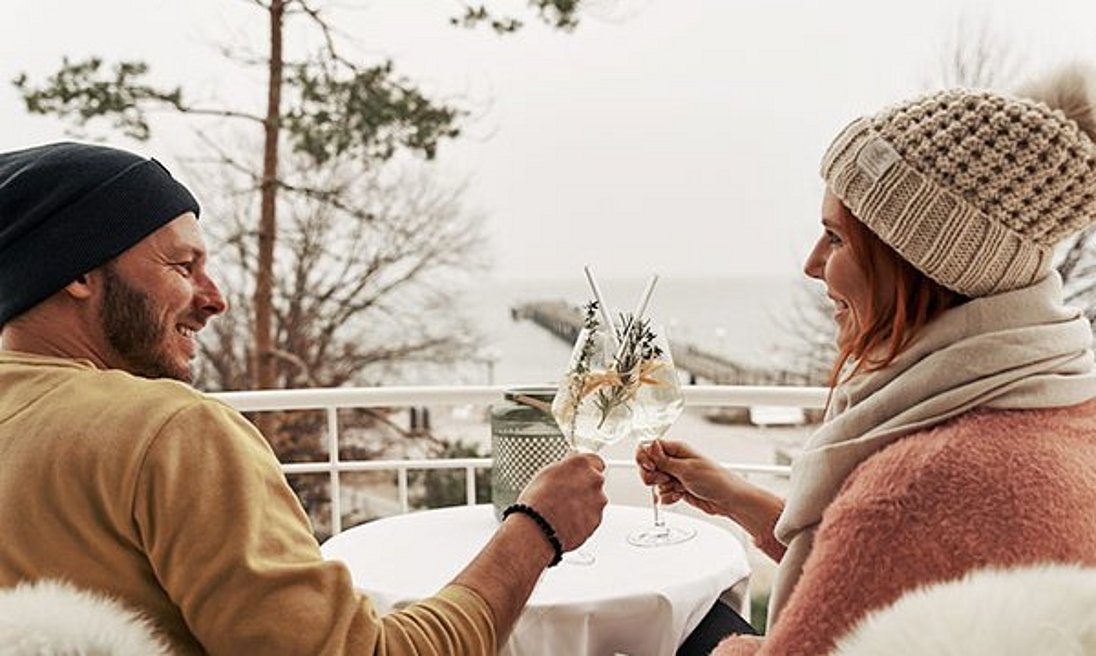 Paar genießt Winterstimmung auf Hotelbalkon mit einem Drink